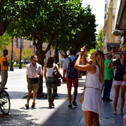 Photo d'une rue avec de nombreux passants. Au premier plan, une femme prenant une photo d'un point d'intérêt dans la ville.